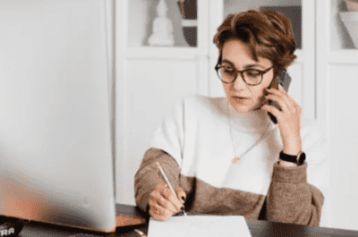 Lady with glasses using a phone and making notes in a notepad. - Wessex Commercial Solutions Xero Accountants in Exeter and Yeovil